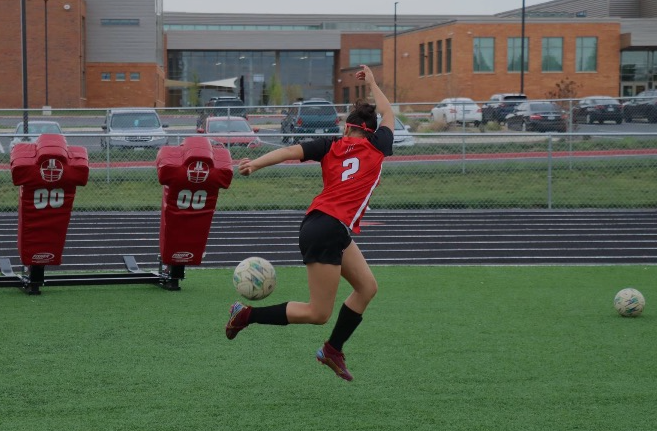Freshman Emily Barahona is in mid-air swinging her right leg to kick the ball while her left arm is raised for balance.