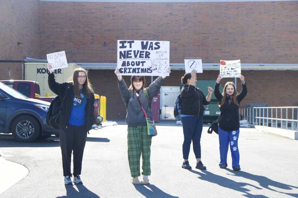 Students display signs while classmates head outside for the walkout.